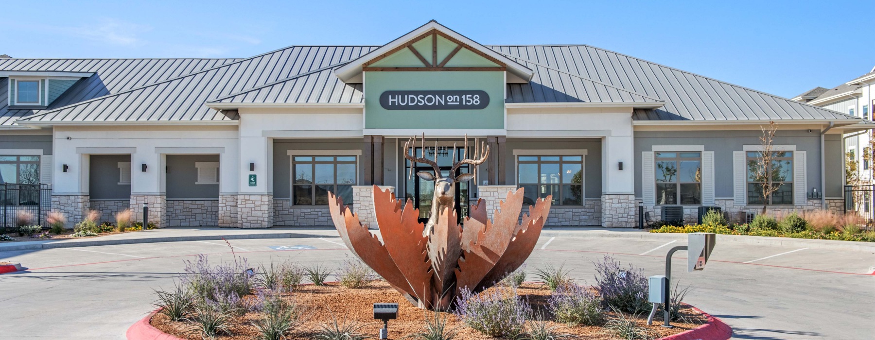 The entrance to our apartments in Midland, TX, featuring a drop off area, a metal sculpture, and a sign reading "The Hudson".
