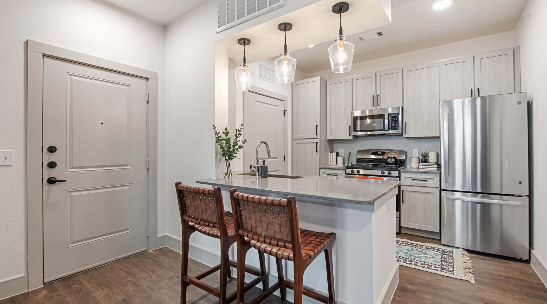 Model living room and kitchen at our apartments in Midland, featuring wood grain floor paneling and counter seating. Model living room and kitchen at our apartments in Midland, featuring wood grain floor paneling and counter seating.