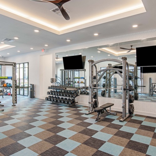 Fitness center at our apartments in Midland, featuring weights, bench presses, a mirrored wall, and televisions.  Fitness center at our apartments in Midland, featuring weights, bench presses, a mirrored wall, and televisions.